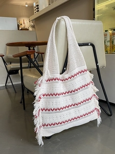 White hand-woven knit tote bag with red stripes and long side fringe on a chair