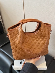 Brown woven leather bucket bag with top handle and crossbody strap in a minimalist style
