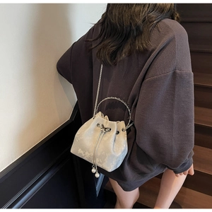 Detail of light grey bucket bag with drawstring closure, pearl charms, and metal ring handle