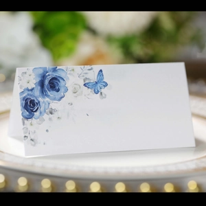 Close-up of a white wedding place card with blue floral and butterfly watercolor print