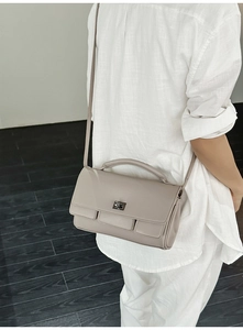 Side view of a taupe crossbody bag featuring a rectangular metal twist lock and top handle