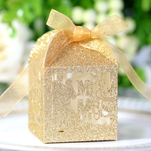 Close-up of golden glitter wedding favor box with Mr & Mrs laser-cut design and ribbon