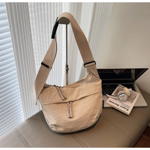 Close-up of beige moon bag with wide strap, buckle detail, and braided zipper pulls