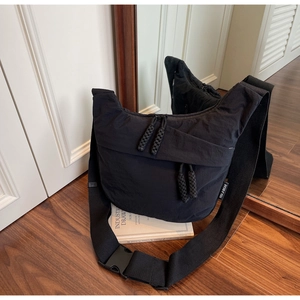 Detail of durable black nylon crossbody bag with woven zipper pull and plastic buckle strap