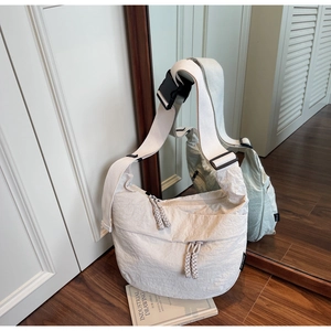 Detail of cream crossbody dumpling bag showing crinkled nylon fabric and woven zipper pull