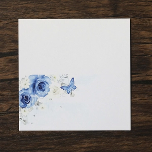 Detailed close-up of wedding place card with blue roses and butterfly on wood background