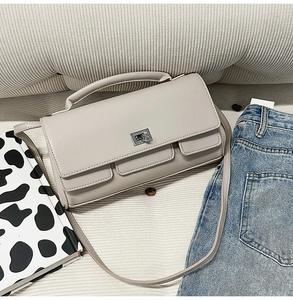 Detail shot of a light grey crossbody bag with silver twist locks on striped fabric