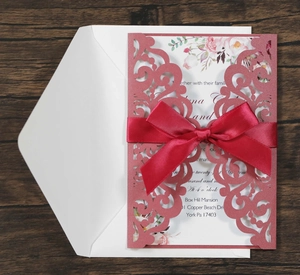 Détail de l'invitation de mariage découpée au laser rose poudré avec nœud en soie rouge