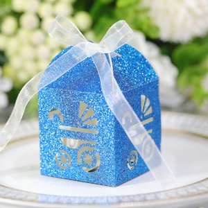 Close-up of blue glitter baby carriage candy box with white ribbon on a white plate