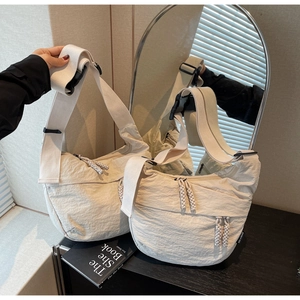 Detail view of cream crossbody bag featuring crinkled nylon fabric and buckle strap