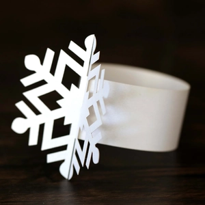 Detailed view of laser-cut white snowflake paper napkin ring on dark wood background