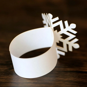 Close-up of laser-cut white paper snowflake napkin rings on a rustic dark wood surface