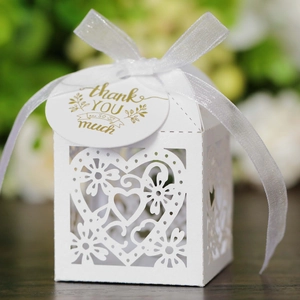 White laser-cut heart wedding favor box with ribbon and thank you tag on wood