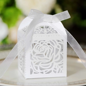 Detail of laser-cut white wedding favor box with rose patterns and a white silk ribbon