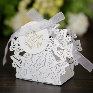 Close-up of white laser-cut butterfly candy box with silk ribbon and gold thank you tag