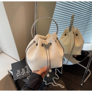 Close-up of beige drawstring bucket bag featuring a butterfly buckle and pearl charms