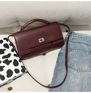 Close-up of wine red rectangular leather bag with silver twist lock on beige fabric
