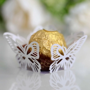 Macro detail of white laser-cut butterfly lace candy wrapper with a gold chocolate ball