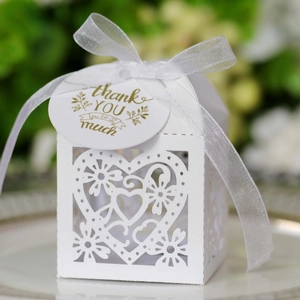 Macro view of white laser-cut wedding favor box with heart patterns and thank you tag