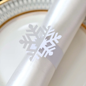 Macro shot of laser-cut white snowflake paper napkin ring on a white napkin with gold-rim plate