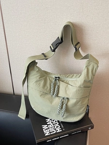 Minimalist green nylon crossbody half-moon bag with thick straps and woven zip pullers