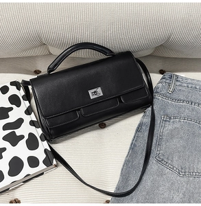 Detail shot of black leather square handbag with silver metal buckle on a textured fabric