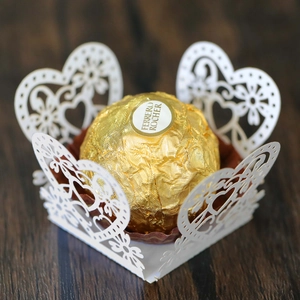 Close-up of laser-cut white heart lace paper liners for chocolate truffles on wood
