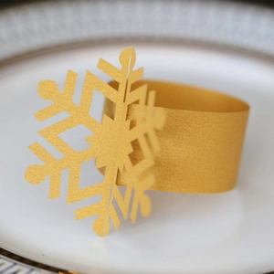 Macro detail of a laser-cut gold snowflake napkin ring on a white ceramic plate