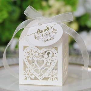 Detail of white laser-cut wedding favor box with heart patterns and gold thank you tag