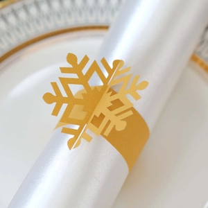 Detailed view of laser-cut gold snowflake paper napkin ring on white silk fabric