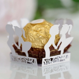 Macro shot of laser-cut white paper lace with boy and girl silhouettes for wedding candy