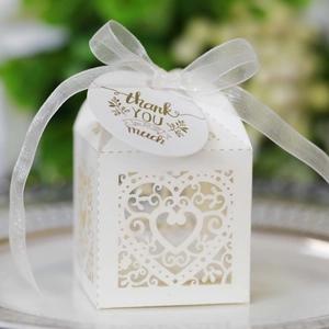 Close-up of laser-cut white wedding favor box with heart patterns and thank you tag