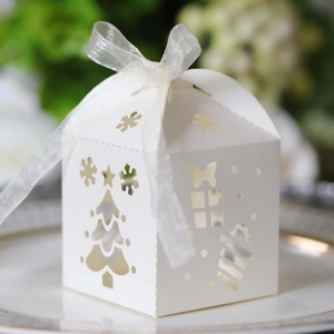 Close-up of white laser-cut Christmas tree and snowflake paper candy box with a ribbon