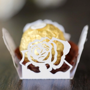 Makroaufnahme der weißen lasergeschnittenen Rosen-Cupcake-Hülle mit Schokolade