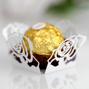 Makroaufnahme weißer, lasergeschnittener Rosen-Papierförmchen für Pralinen und Hochzeit