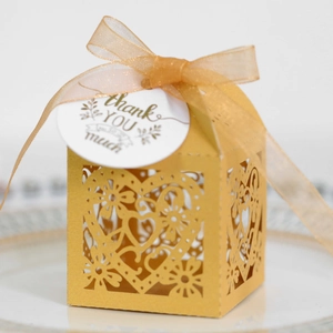 Detail of laser-cut heart pattern on gold favor box with ribbon and thank you tag