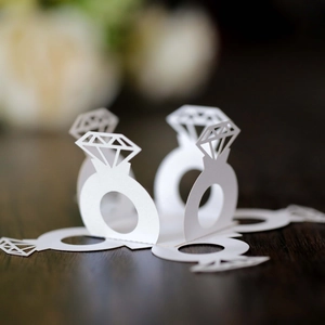 Detail of laser-cut white cardstock diamond ring favors on dark wooden background