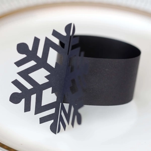 Macro detail of black cutout snowflake napkin ring on elegant gold-rimmed white plate