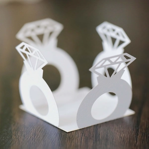 Detailed laser-cut white paper wedding rings decor on a dark wood background