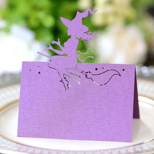 Macro detail of purple laser-cut witch silhouette seat card on white dinner plate