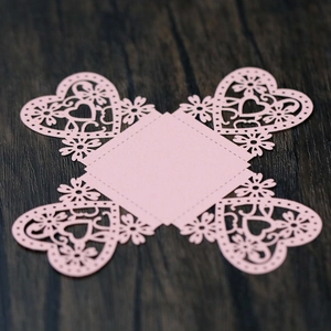 Flat lay of laser-cut pink paper heart box template on a rustic dark wood surface