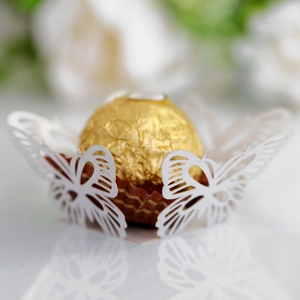 Macro detail of white laser-cut butterfly cupcake wrapper with gold chocolate accent