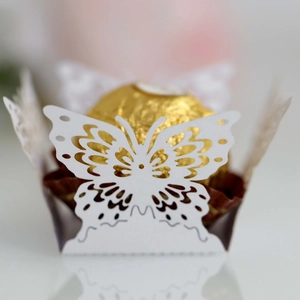 Macro shot of white laser-cut butterfly chocolate holder with a golden truffle inside