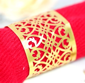 Macro shot of gold laser-cut napkin ring with ornate scroll patterns on red fabric