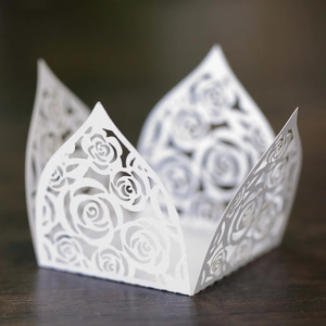 Macro shot of white laser-cut paper cupcake wrappers with intricate rose flower pattern
