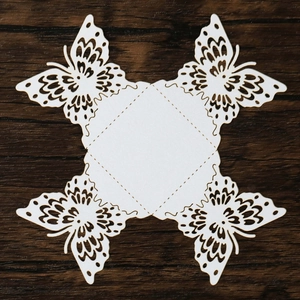 Flat lay of laser-cut white butterfly paper favor box with intricate hollow lace details