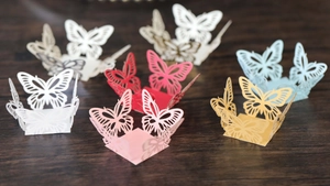 Detail of laser-cut butterfly paper cake toppers in various colors on wooden surface