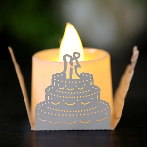 Macro detail of laser-cut paper candle wrap with warm LED light showing a wedding cake design