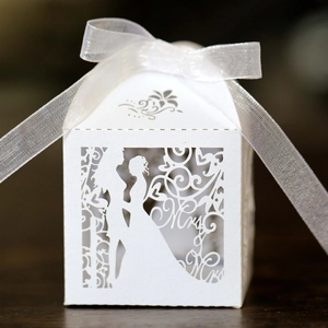 Close-up of laser-cut white wedding favor box with Mr & Mrs silhouette and silk ribbon