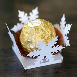 Close-up of laser-cut white snowflake chocolate holder on a dark wooden table background